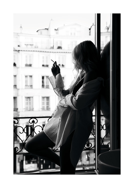  – Mustavalkoinen valokuva naisesta isossa kauluspaidassa polttamassa savuketta ikkunalla