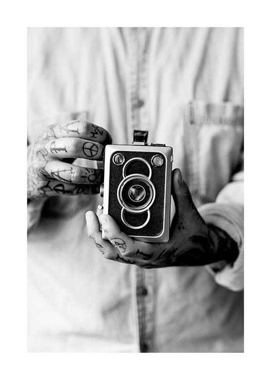  – Mustavalkoinen valokuva vintage-kamerasta, jota pitelevät miehen tatuoidut kädet