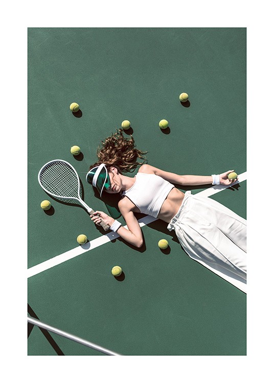 -Valokuva tytöstä valkoisissa housuissa ja topissa makaamassa tenniskentällä tennispallojen ympäröimänä
