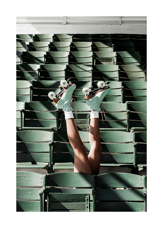  – Valokuva henkilöstä rullaluistimissa venyttelemässä jalkojaan vihreiden stadionistuimien välissä