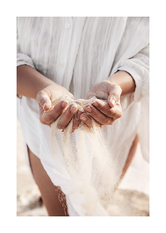  – Valokuva naisesta hiekkaa käsissään, valkoinen pellavapaita taustanaan