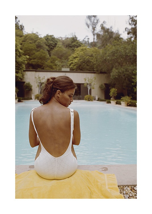  – Valokuva naisesta, joka istuu pyyhkeellä uima-altaan edessä valkoisessa uimapuvussa