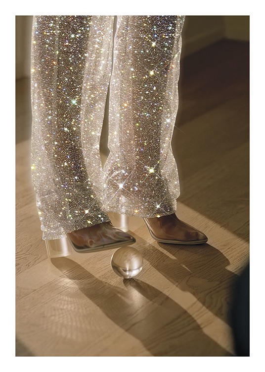  – Valokuva naisesta lasipallo jalkansa alla yllään kimaltavat housut