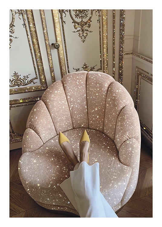  – Valokuva vaaleanpunaisesta kimaltavasta nojatuolista kultaisen ja valkoisen seinän edessä ja naisesta jalat tuolilla