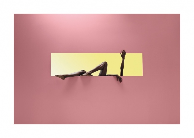  – Valokuva naisesta keltaisessa suorakulmiossa vaaleanpunaista taustaa vasten, ulos ojennetuin käsin ja jaloin