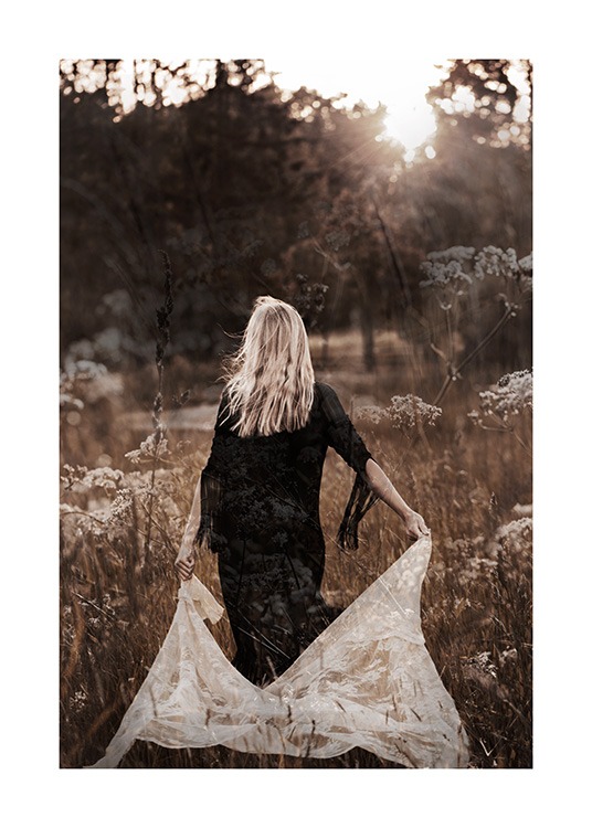  – Valokuva niityllä kulkevasta naisesta mustassa mekossa ja valkoinen pitsikangas takanaan