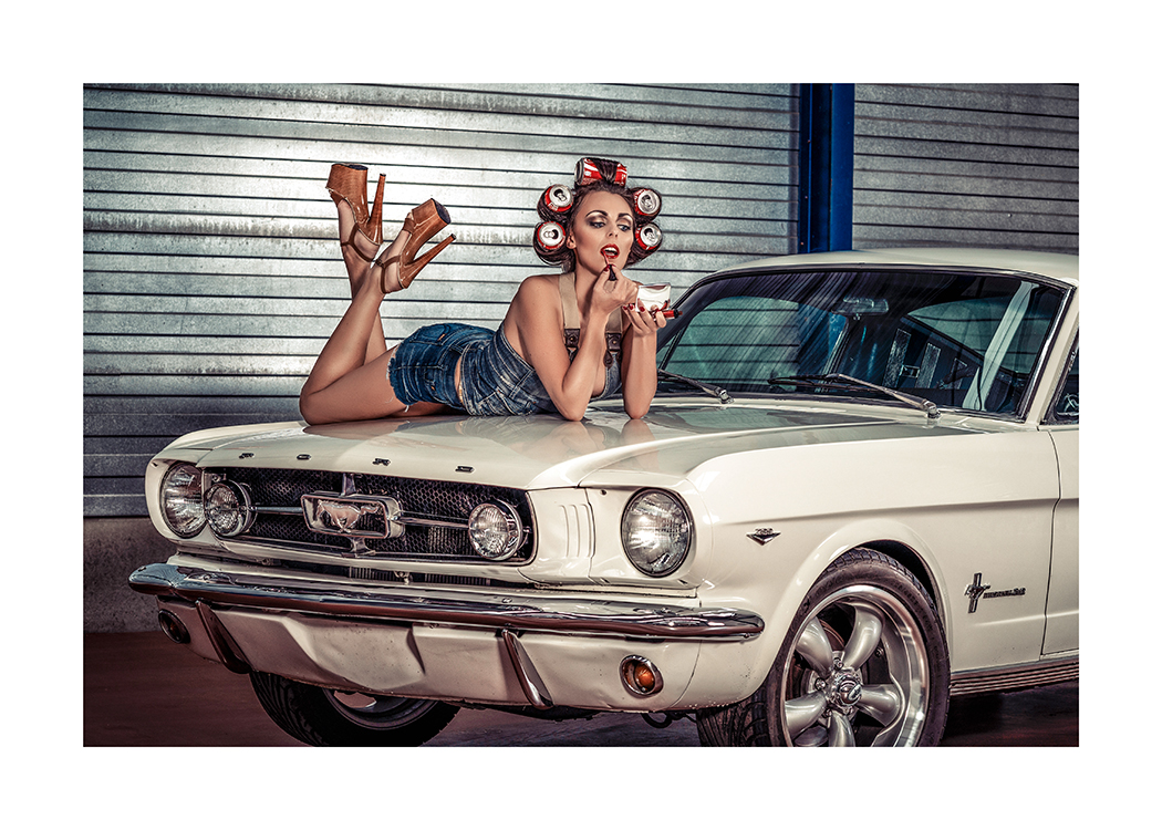  – Valokuva naisesta limsatölkit hiuksissaan makaamassa auton konepellillä ja levittämässä huulipunaa huulilleen