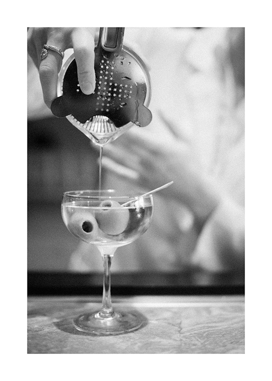  – Mustavalkoinen valokuva juomaravistimesta kaadetusta martinista ja oliiveista lasissa