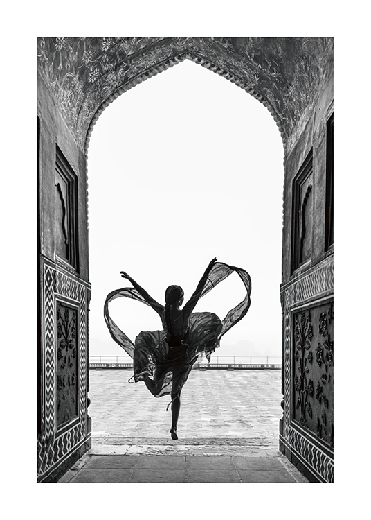  – Mustavalkoinen valokuva naisesta tanssimassa yhdellä jalalla lainehtivassa mekossa kaaren alla