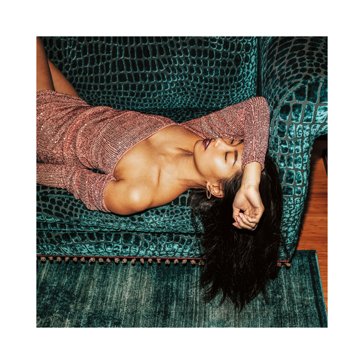  – Valokuva naisesta kimaltelevassa mekossa nokosilla turkoosilla sohvalla