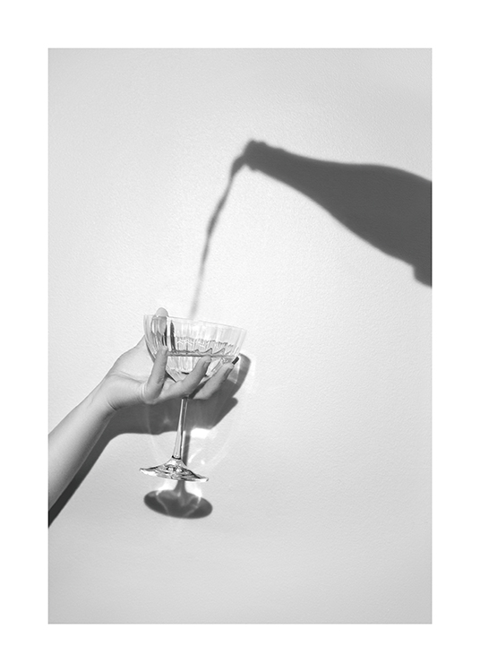  – Harmaa valokuva samppanjapullon varjosta ja samppanjalasia pitelevästä kädestä