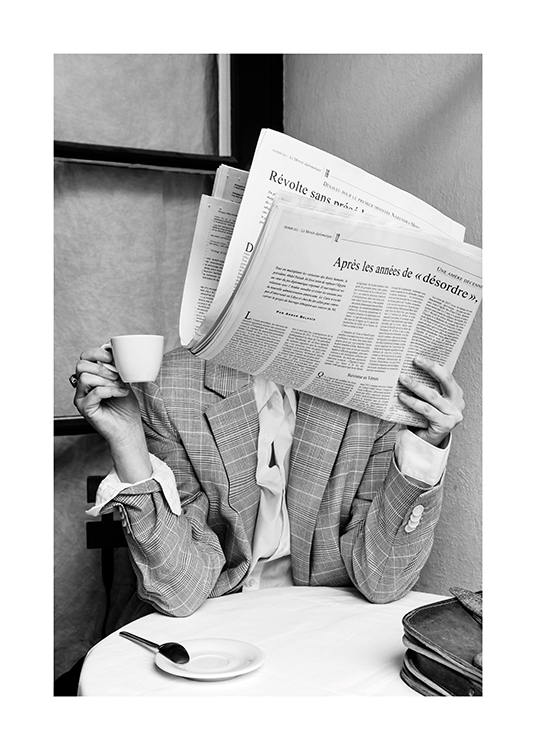  – Mustavalkoinen valokuva kahvilan pöydässä istuvasta henkilöstä sanomalehti kasvojensa edessä