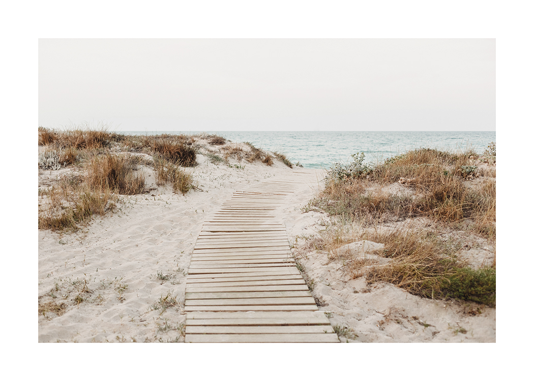  – Valokuva hiekkadyyneistä ja niitä reunustavista heinistä, puisesta kulkureitistä ja merestä taustalla