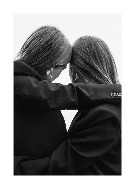  – Mustavalkoinen valokuva kahdesta naisesta puvuissa nojaamassa päitään yhteen