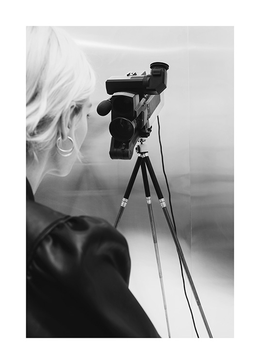  – Mustavalkoinen valokuva vaaleahiuksisesta naisesta videokamerajalustan takana