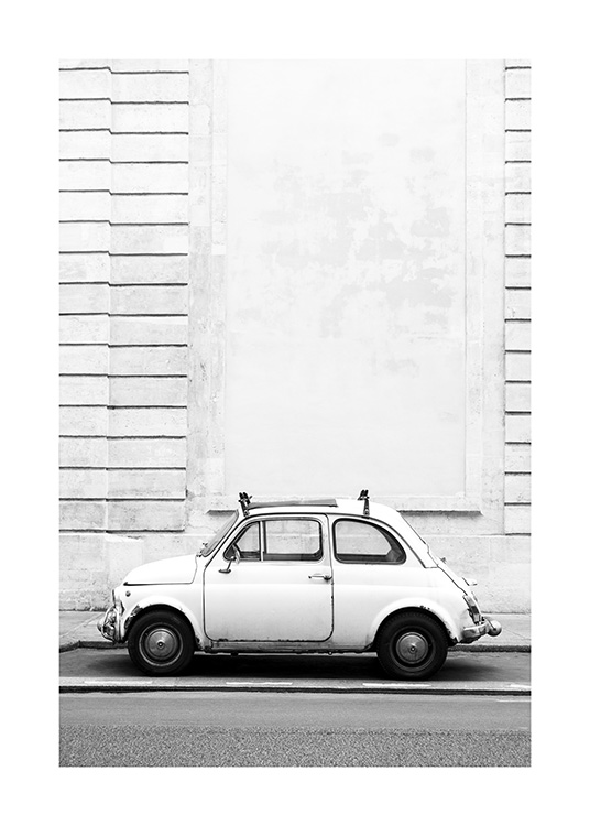  – Mustavalkoinen valokuva pienestä retroautosta rakennuksen raidallisen seinän edessä